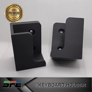 May include: Two black plastic keyboard holders. The holders are designed to be mounted to a wall or desk. The holders are made of a durable plastic and have a simple design.