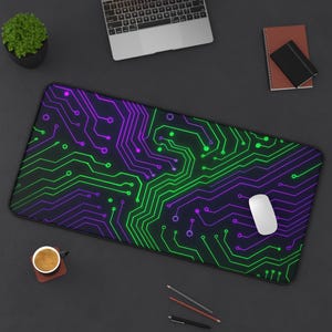 May include: A rectangular black mousepad with a vibrant circuit board design in neon green and purple. A white computer mouse rests on the pad. The pad is on a dark surface with a laptop, coffee cup, and stationery.
