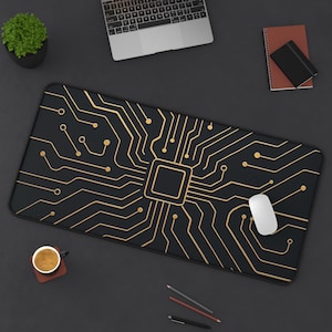 May include: Black rectangular mousepad with a gold circuit board design. A white computer mouse rests on the pad. Other items on the dark surface include a laptop, a small potted plant, a notebook, and a cup of coffee.