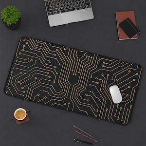 Puede incluir: Una alfombrilla de ratón rectangular negra con un diseño de placa de circuito dorado. Un ratón de ordenador blanco está sobre la alfombrilla. Un portátil, una pequeña planta en maceta, un cuaderno y una taza de café también están sobre la superficie oscura.