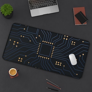 May include: Black rectangular mousepad with a blue and gold circuit board design. A white computer mouse sits on the pad. Other items on the dark surface include a laptop, a small potted plant, a coffee cup, a notebook, and writing utensils.