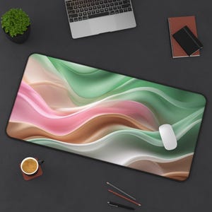 May include: A large rectangular mouse pad with a black border. The pad features a flowing abstract design in shades of pink, green, brown, and white. A white computer mouse rests on the pad.