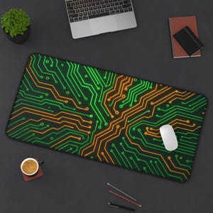 May include: A rectangular computer mouse pad with a circuit board design in neon green and orange on a black background. A white computer mouse rests on the pad. A laptop, coffee cup, and other office supplies are also visible.