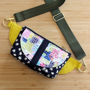 Può includere: Una marsupio nera e gialla con stampa a stelle e un design patchwork colorato. La borsa ha una tracolla regolabile verde con accessori dorati.