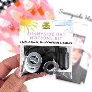 May include: A Sunnyside Hat Notions Kit in a clear plastic bag containing three sets of black elastic, black barrel cord locks, and silver metal washers. The header card features the text Sunnyside Hat Notions Kit and 3 Sets of Elastic, Barrel Cord Locks & Washers.