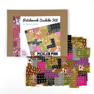 May include: A craft kit labeled "Patchwork Sashiko Kit" by BanjoFlannel. The kit includes a brown cardboard box with a colorful patchwork design and the words "PICKLED PINK". A collection of fabric squares in various colors and patterns are displayed.