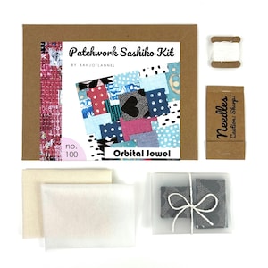 May include: A Patchwork Sashiko Kit by Banjoflannel, no. 100, Orbital Jewel. Includes a brown envelope with a patterned label, a spool of white thread, a brown packet labeled Needles Caution: Sharp!, two folded cream fabric pieces, and gray fabric.