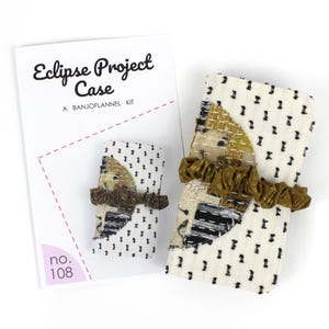 Pode incluir: Um kit Eclipse Project Case da BANJOFLANNEL. O kit inclui uma caixa pequena e grande com fundo creme e padrão de pontos pretos. As caixas têm um design de patchwork com babados verde-oliva e o texto "Eclipse Project Case" na embalagem.