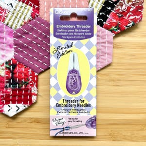 May include: A Clover brand embroidery threader in a purple plastic casing with a clover leaf design, packaged on a rectangular card with a yellow and white checkered pattern. The packaging features the text Embroidery Threader and Limited Edition.