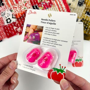 May include: A pack of Dritz needle pullers. The package contains two bright pink silicone needle pullers in a clear plastic blister pack. The package also includes the text "Needle Pullers Tireur d'aiguille".