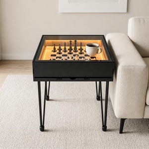 Pode incluir: Mesa de xadrez preta com tampo de vidro, com um tabuleiro de xadrez iluminado e peças de xadrez. A mesa tem uma gaveta e pernas de metal pretas. Uma caneca branca está sobre a mesa.