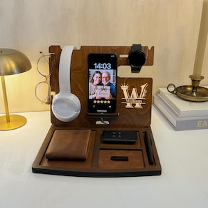 Könnte beinhalten: Eine hölzerne Ladestation mit mehreren Fächern. Sie enthält ein Telefon mit Foto, eine Brille, eine Uhr, Kopfhörer, eine Brieftasche und einen Stift. Die Station ist mit dem Namen "William" graviert.