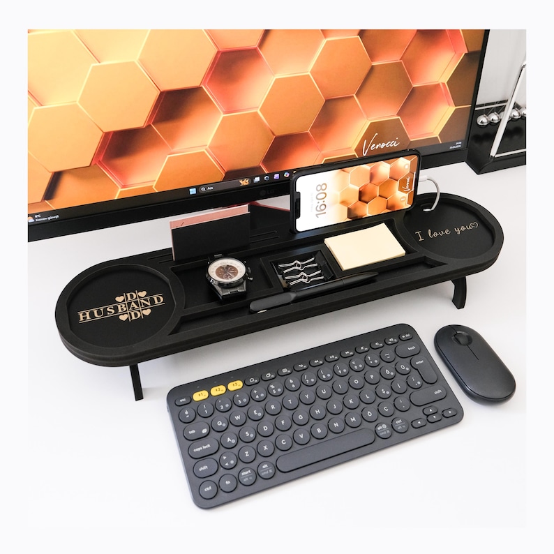 K&ouml;nnte beinhalten: Ein schwarzer Schreibtisch-Organizer mit Telefon, Uhr, Stift und Notizblock. Der Organizer hat eine Tastatur, eine Maus und die Worte "I love you?" und "D HUSBAND D". Der Hintergrund ist ein Computermonitor.