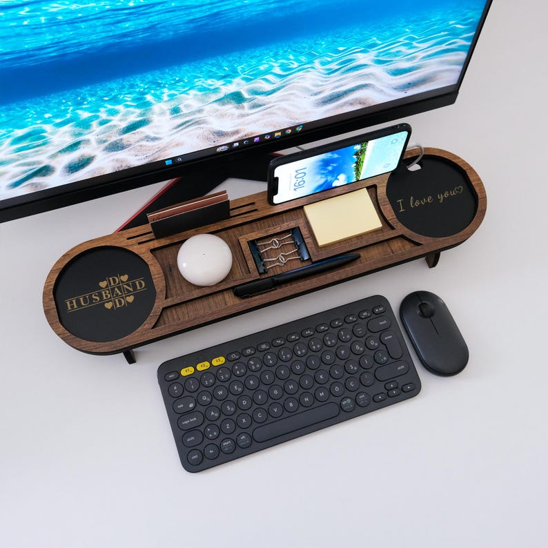 K&ouml;nnte beinhalten: Ein dunkler Schreibtisch-Organizer aus Holz mit F&auml;chern f&uuml;r ein Telefon, Stifte und einen Notizblock. Eine schwarze Tastatur, Maus und ein Computermonitor sind ebenfalls zu sehen. Der Organizer tr&auml;gt die Worte "Husband" und "I love you".