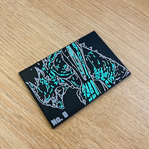 May include: A black rectangular patch featuring an abstract design in light blue and grey. The patch has the number "No. 8" printed in white. The design appears to be a stylized illustration.