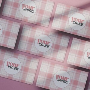 Può includere: Biglietti da visita a quadri rosa e bianchi con la scritta "YOUR LOGO HERE" in un cerchio. I biglietti sono disposti in diagonale su una superficie rosa, con ombre.