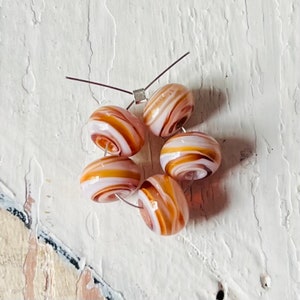 May include: Six white and brown swirl glass beads with a silver wire threaded through them.