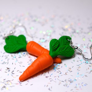 May include: A pair of carrot earrings with green leafy tops. The earrings are made of polymer clay and have silver hooks.
