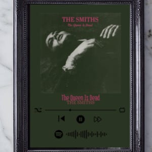 May include: A framed print of The Smiths' "The Queen Is Dead" album cover. The artwork features a dark green backdrop with pink text. The black frame has an ornate design. The image includes a music player interface.