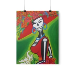 Può includere: Un dipinto colorato di una donna scheletro che indossa un cappello rosso con fiori e un vestito rosso. Tiene un fiore bianco in mano.