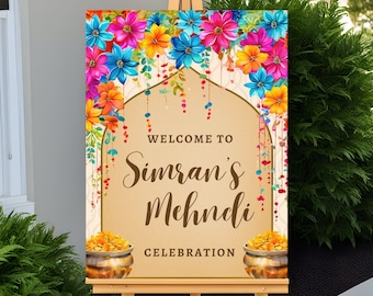 May include: A welcome sign for a Mehndi celebration with a floral archway and gold pots. The sign reads "Welcome to Simran's Mehndi Celebration."