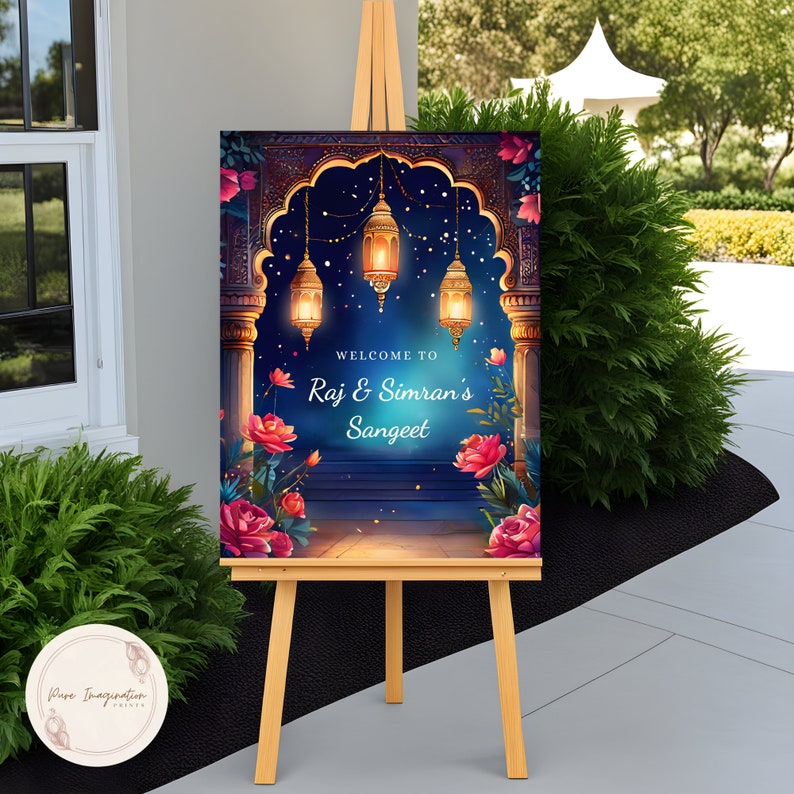 May include: A welcome sign for a Sangeet celebration with a blue and gold archway decorated with hanging lanterns and floral accents. The sign reads "Welcome to Raj & Simran's Sangeet".