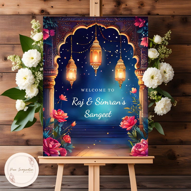 May include: A welcome sign for a Sangeet celebration with a blue and gold archway decorated with floral accents and lanterns. The sign reads "Welcome to Raj & Simran's Sangeet".