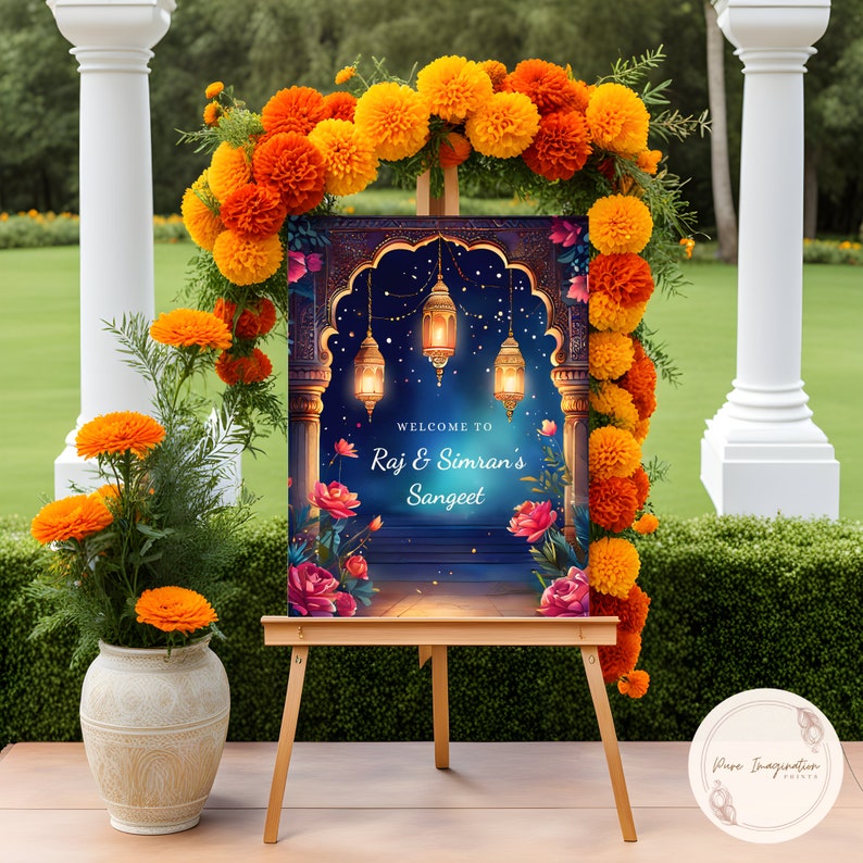 May include: A welcome sign for a Sangeet celebration with a blue and gold archway design, featuring lanterns and floral accents. The sign reads "Welcome to Raj & Simran's Sangeet".