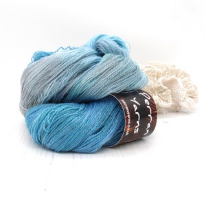May include: Two skeins of blue yarn in varying shades, from light blue to teal, are displayed. A brown label with white text reading "Perran Yarns" is visible. A white, coral-like decorative object is in the background. The yarn is on a white surface.