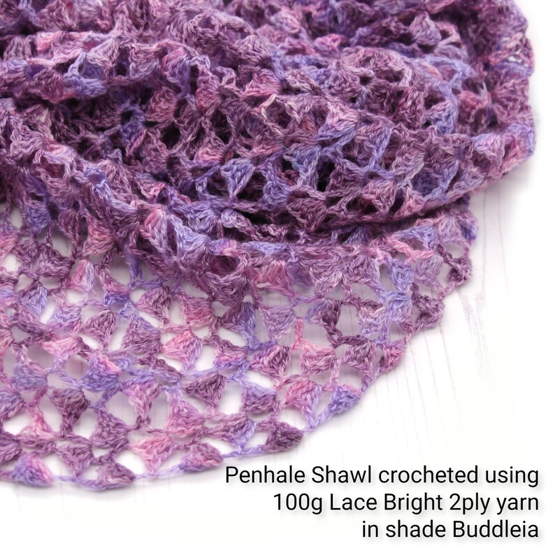 May include: A close-up of a crocheted shawl in shades of purple, lavender, and pink. The openwork design is made with 100g Lace Bright 2ply yarn in the shade Buddleia. The text "Penhale Shawl" is visible.