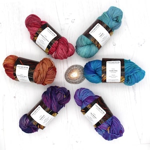 May include: Six skeins of hand-dyed yarn in various colors, including cranberry, cinnamon spice, lagoon, scuba dive, starburst, and sky rocket. Each skein is labeled "Cozy Eight De Soie" with the color name.