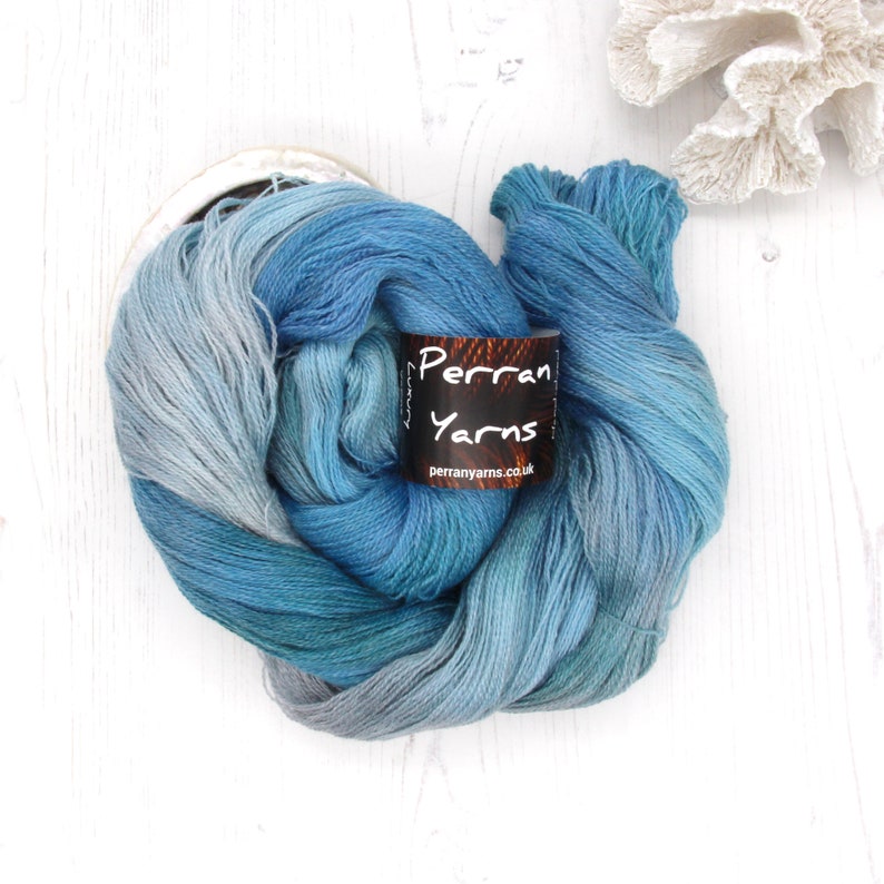 May include: A skein of blue and teal yarn with a label that reads "Perran Yarns". The yarn is a gradient of colors, ranging from light blue to deep teal. The label also includes the website perranyarns.co.uk.