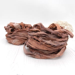 May include: A close-up of a pile of brown silk ribbon. The ribbon is frayed and has a rustic look.