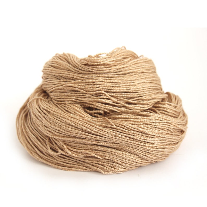 Puede incluir: Primer plano de una madeja de hilo beige. El hilo es suave y esponjoso, y es perfecto para tejer o hacer ganchillo.
