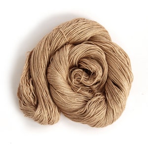 Puede incluir: Un ovillo de hilo beige, hecho de fibras naturales, est&aacute; enrollado en forma de bola de forma suelta.