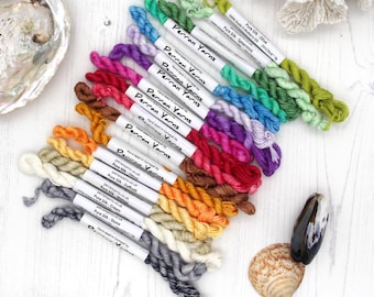 May include: A collection of Perran Yarns Pure Silk embroidery threads in a spectrum of colors, including olive, spearmint, purple, pink, red, orange, yellow, cream, stone, and grey, each with a white label detailing the specific color name.