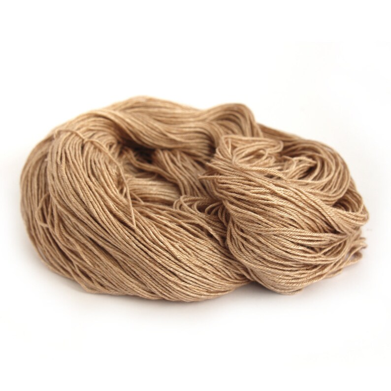 Puede incluir: Una madeja de hilo de color marr&oacute;n claro, hecha de fibras naturales, est&aacute; amontonada sin apretar sobre una superficie blanca.