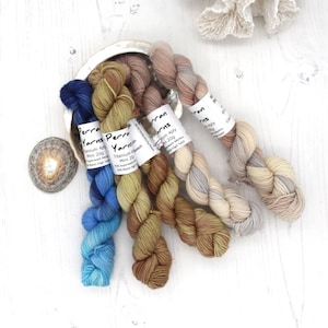 May include: Five skeins of yarn in different colours, including blue, brown, beige, and grey. The yarn is labelled "Perran Yarns" and includes the yarn weight, fibre content, and yardage.