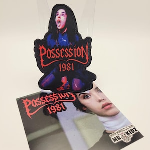 May include: A black patch featuring a distressed image of a woman with the text "Possession 1981" in red. A matching card with the same text and a close-up of a woman's face is also visible.