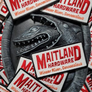 May include: Close-up of several white and red embroidered patches with the text "Maitland Hardware Winter River, Connecticut".