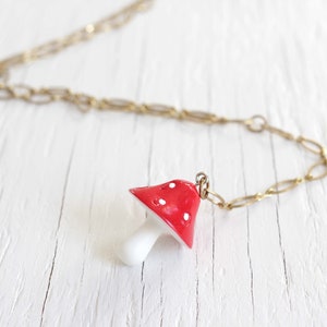 May include: A gold chain necklace with a red and white mushroom pendant. The mushroom has white dots on the red cap.