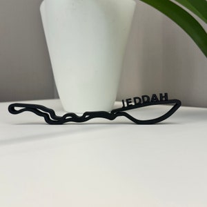 Könnte beinhalten: Schwarz 3D-gedrucktes Modell der Rennstrecke Jeddah Corniche Circuit mit dem Wort "Jeddah" auf der Strecke.