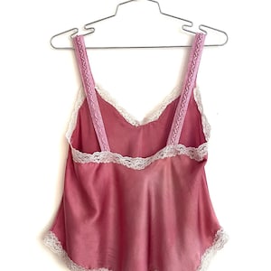 May include: A pink satin camisole with white lace trim. The camisole has adjustable straps and a scoop neck.