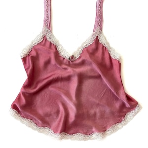 May include: A pink satin camisole with white lace trim. The straps are made of a woven fabric.