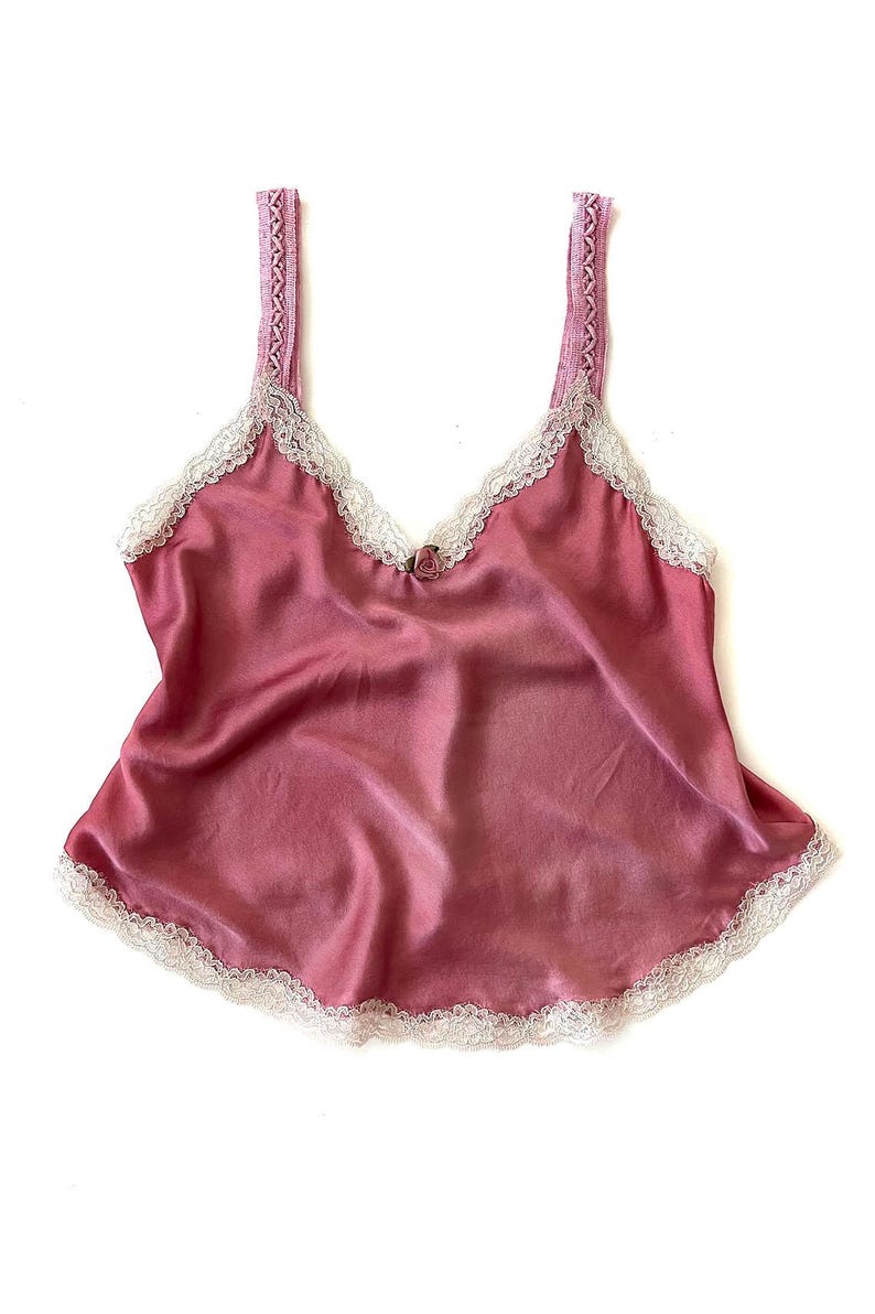 May include: A pink satin camisole with white lace trim. The straps are made of a woven fabric.