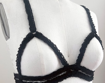 Pode incluir: Bralette de renda preta com design de gaiola. O sutiã apresenta delicadas bordas de renda ao longo das bordas e alças. O bralette é exibido em um manequim branco, mostrando seus detalhes e construção intrincados. A lingerie é projetada para conforto e estilo.