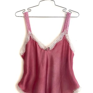 May include: A pink satin camisole with white lace trim. The camisole has thin straps and a V-neckline.