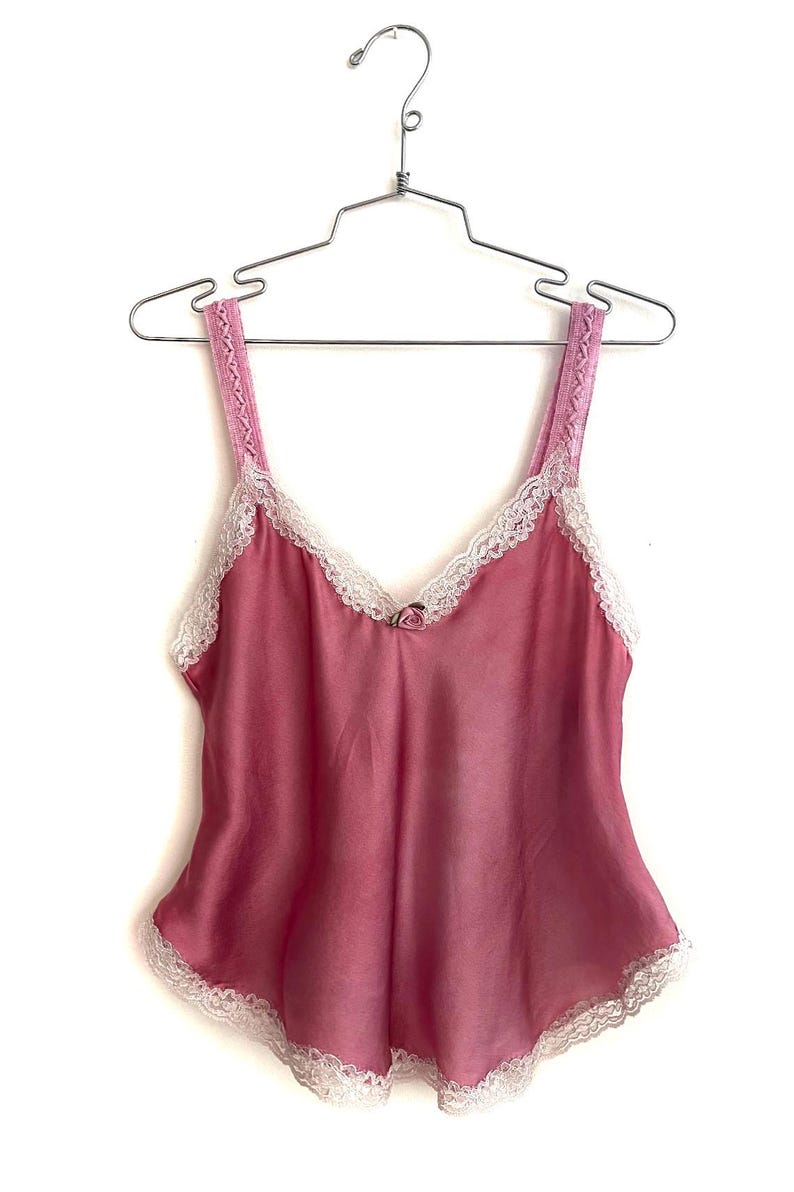 May include: A pink satin camisole with white lace trim. The camisole has thin straps and a V-neckline.