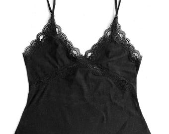 May include: Black camisole with delicate lace trim along the neckline and straps. The top features a ribbed texture and a scalloped hemline. A simple, elegant design.