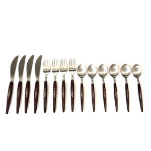 Puede incluir: Un juego de cubiertos antiguos, que incluye cuchillos, tenedores y cucharas. Los utensilios de acero inoxidable tienen mangos de color marrón oscuro con un diseño floral. El juego está dispuesto sobre una superficie blanca.